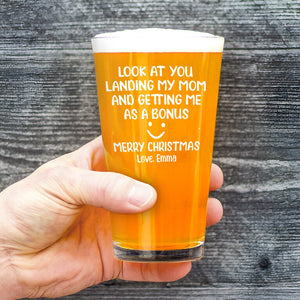 Hand holding engraved pint glass with Merry Christmas message filled with amber beer and foam Personalized Whiskey Glass
