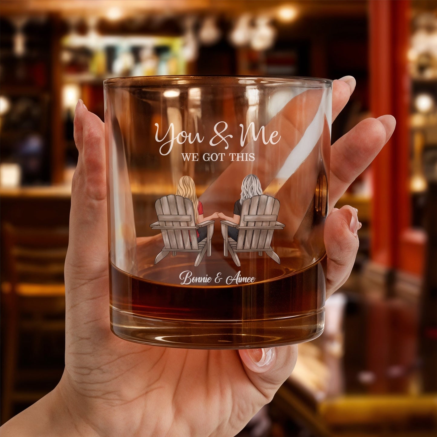 Hand holding a personalized couple whiskey glass with two people in Adirondack chairs You and Me message and custom names