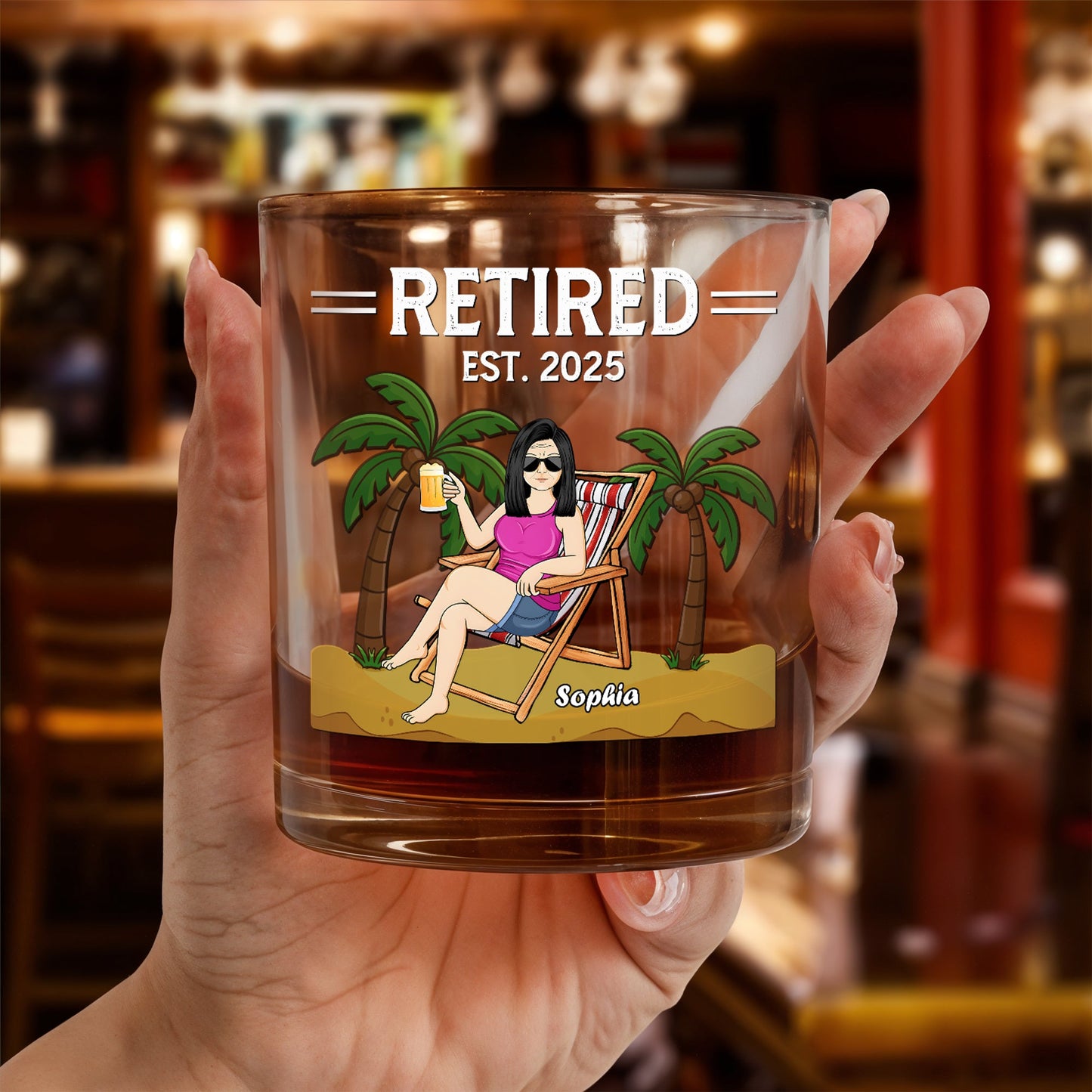 Personalized Whiskey Glass held in hand featuring retired est 2025 design with woman lounging and palm trees