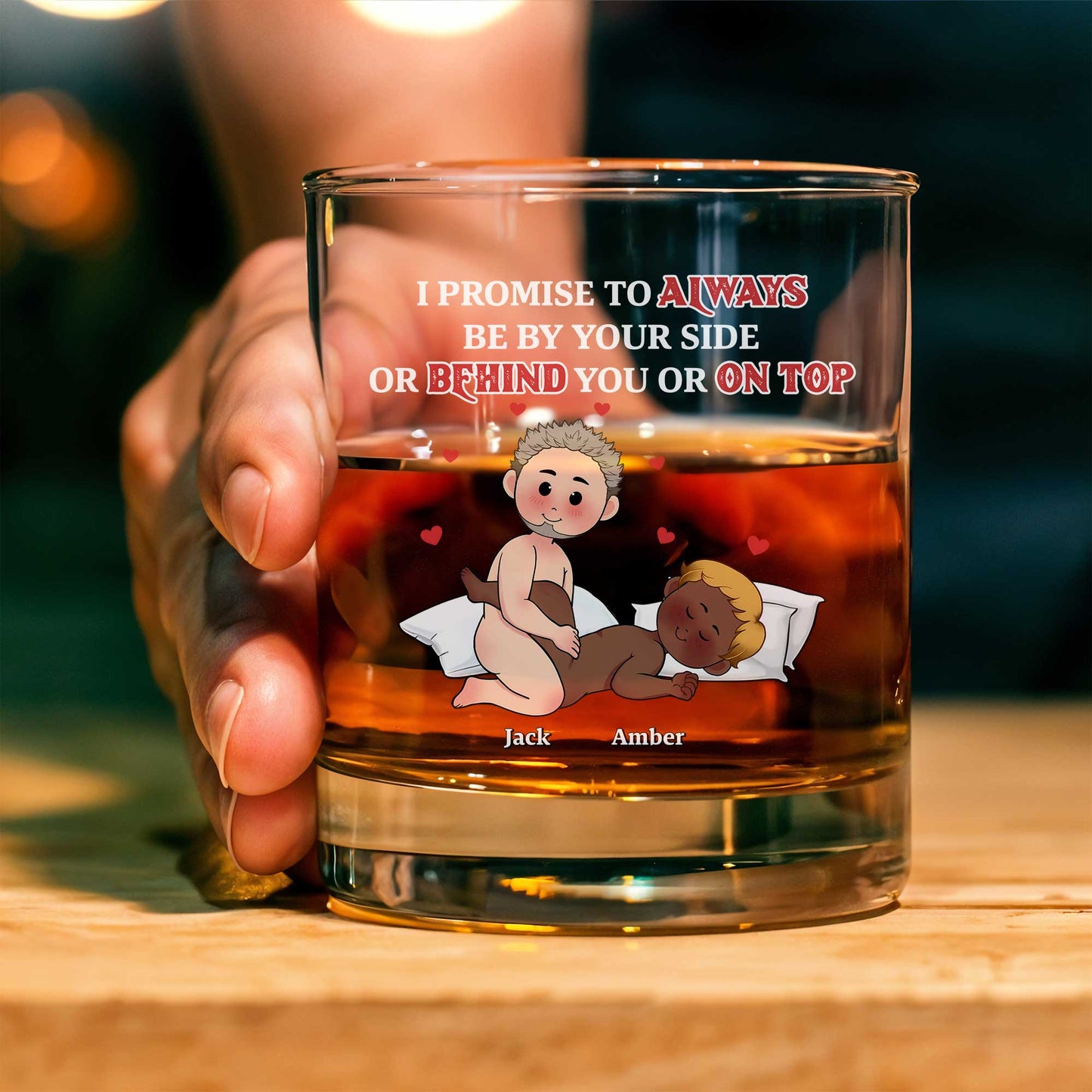 Hand holding a personalized couple whiskey glass with cartoon partners in bed custom names Jack and Amber and promise text