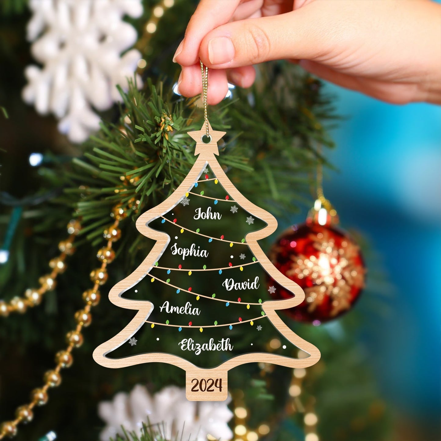 Hand holding a personalized Christmas tree ornament made of wood with names and 2024 on decoration