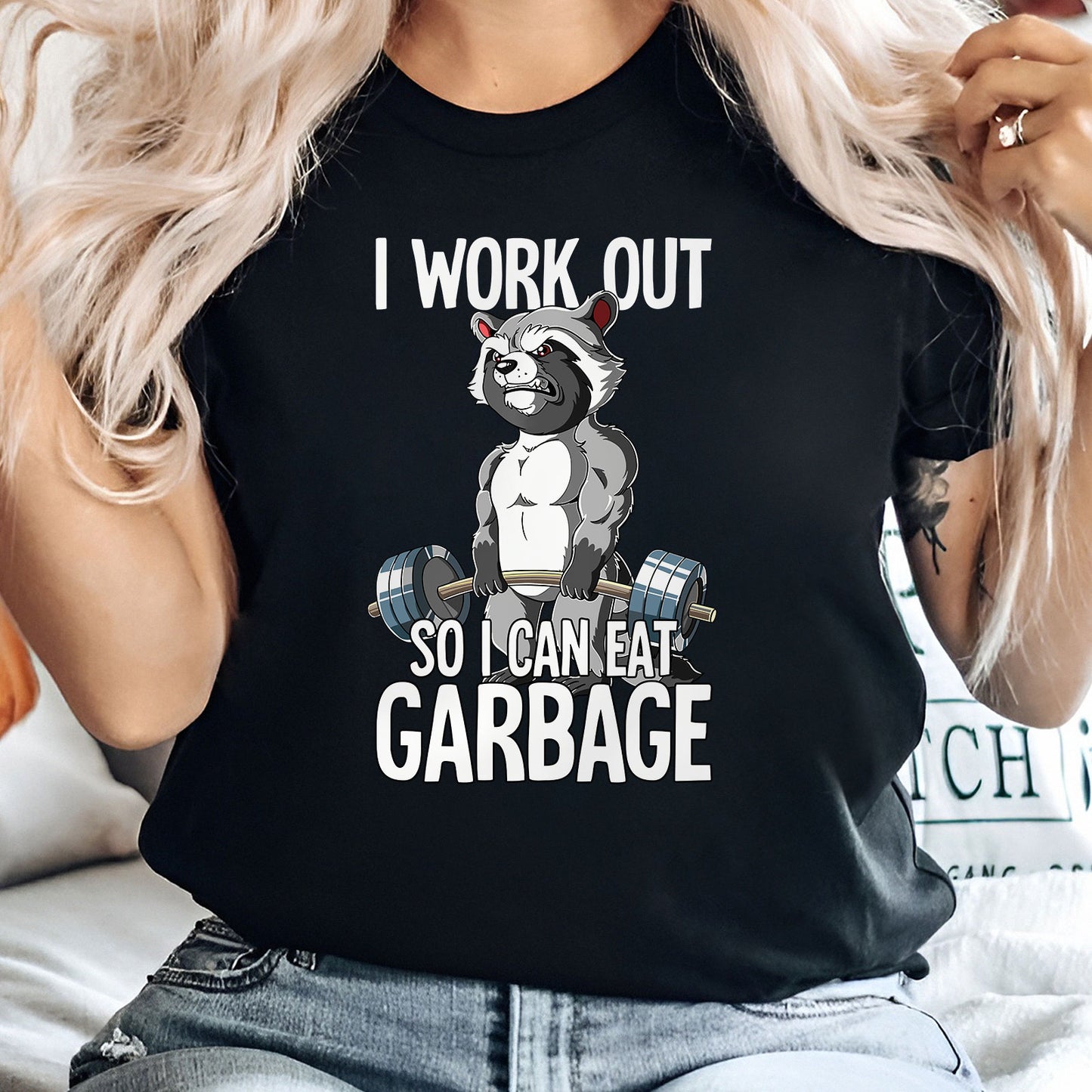 Humorous workout apparel black t-shirt featuring muscular raccoon lifting weights with text I work out so I can eat garbage