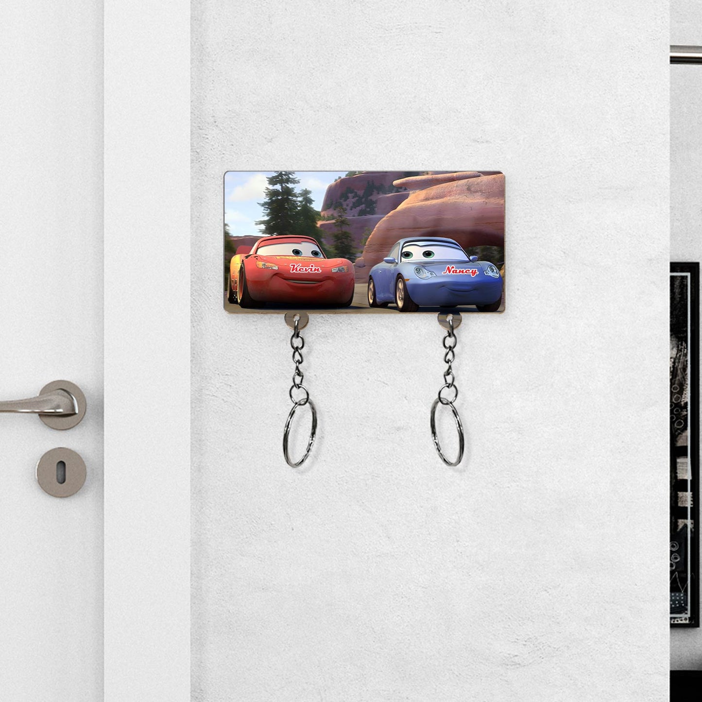 Personalized couple key holder featuring red and blue cartoon cars with custom names mounted on white wall