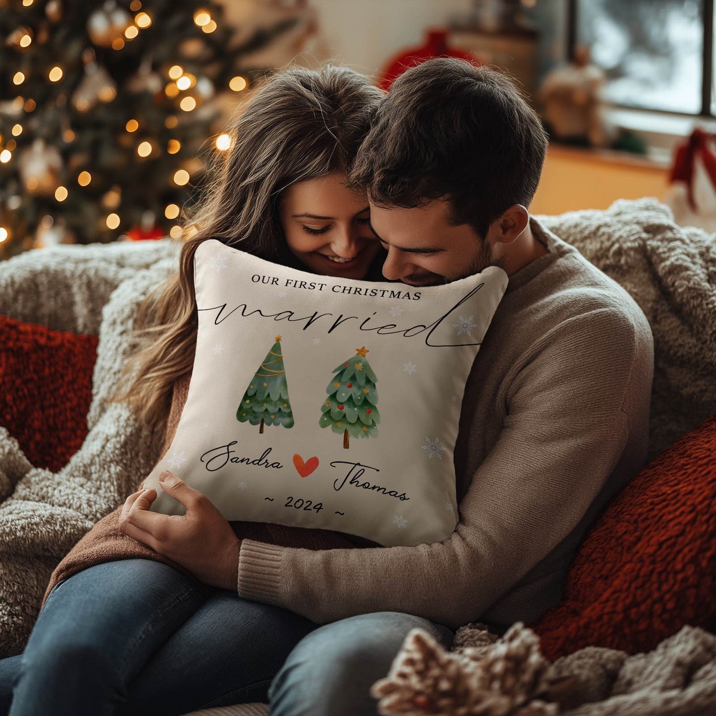 Couple sitting on cozy couch holding personalized first Christmas married pillow with tree design
