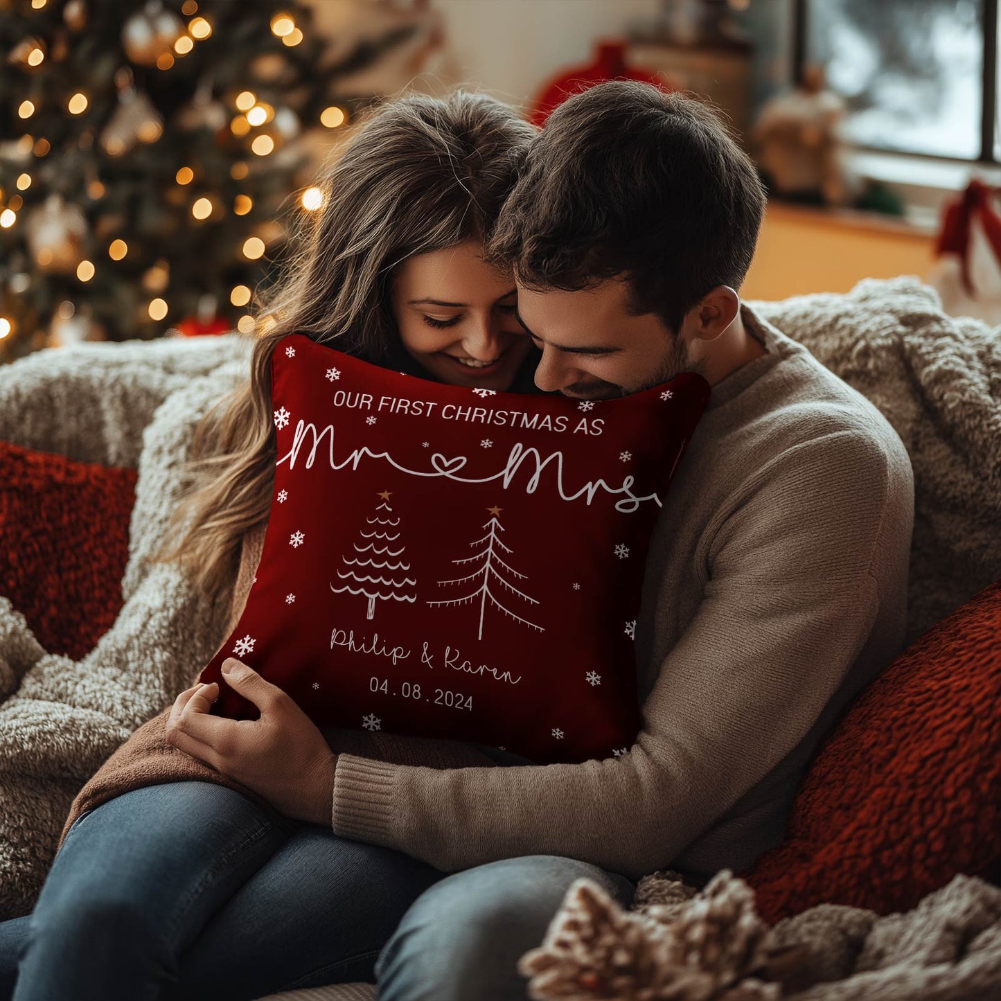 Couple hugging a personalized first Christmas pillow with names and date in a cozy festive living room