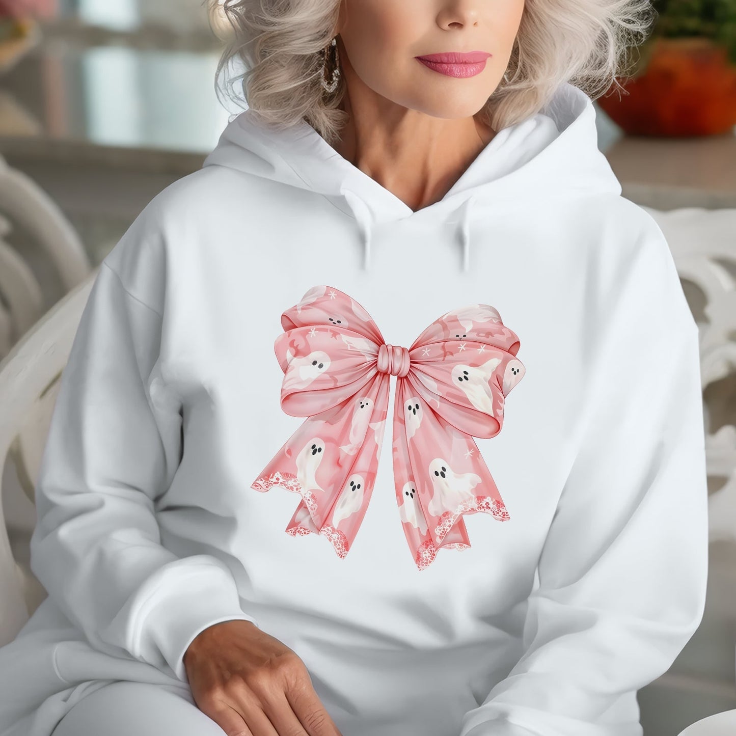 Woman wearing white hoodie with personalized pink Halloween shirt design featuring a large pink bow with ghost patterns