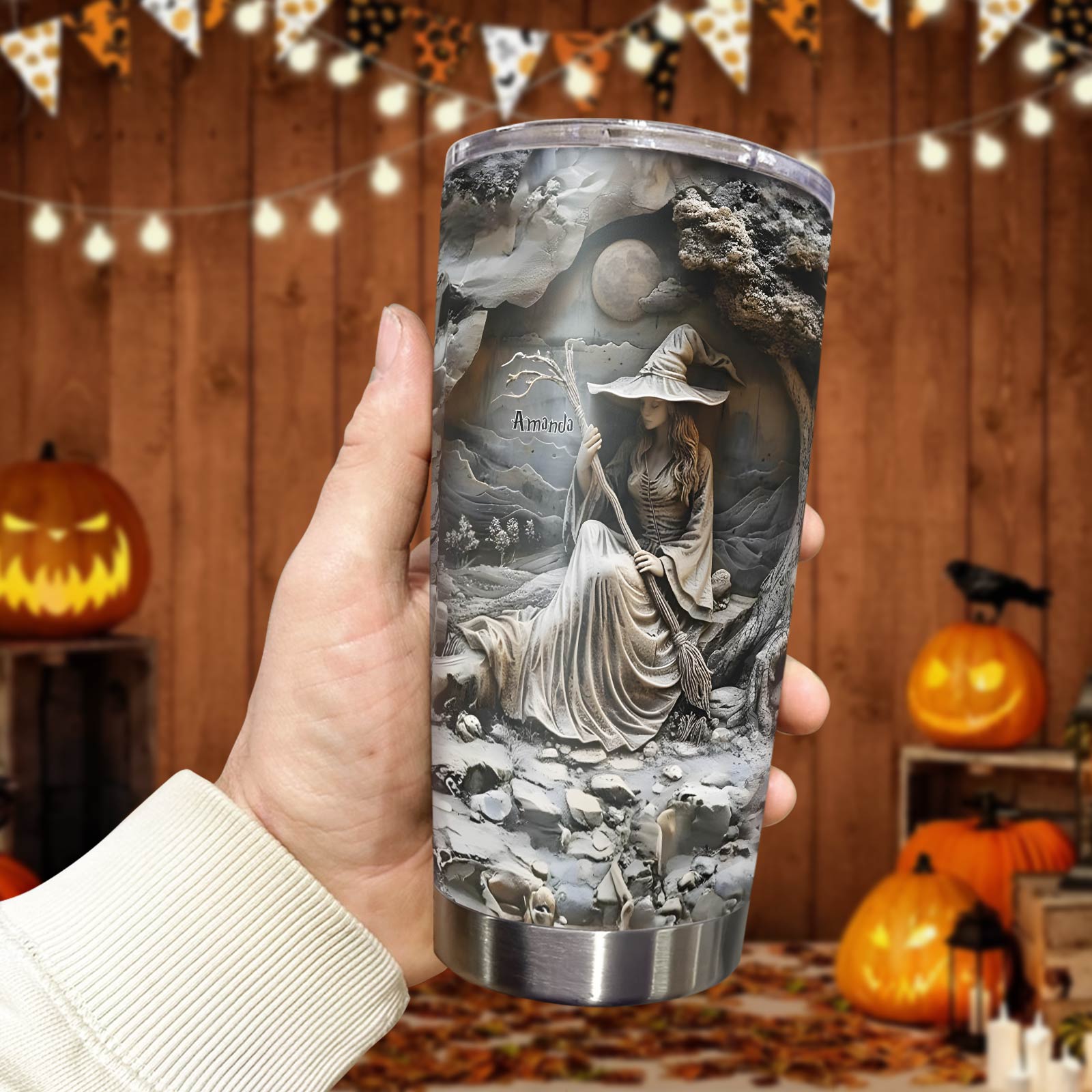 Hand holding a personalized witch tumbler featuring a detailed witch design engraved with the name Amanda
