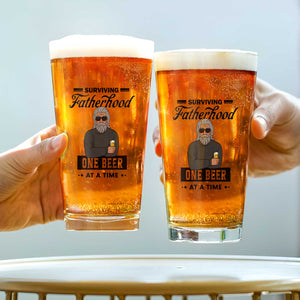 Personalized Whiskey Glass novelty pint glasses featuring Surviving Fatherhood One Beer at a Time graphic two hands clinking