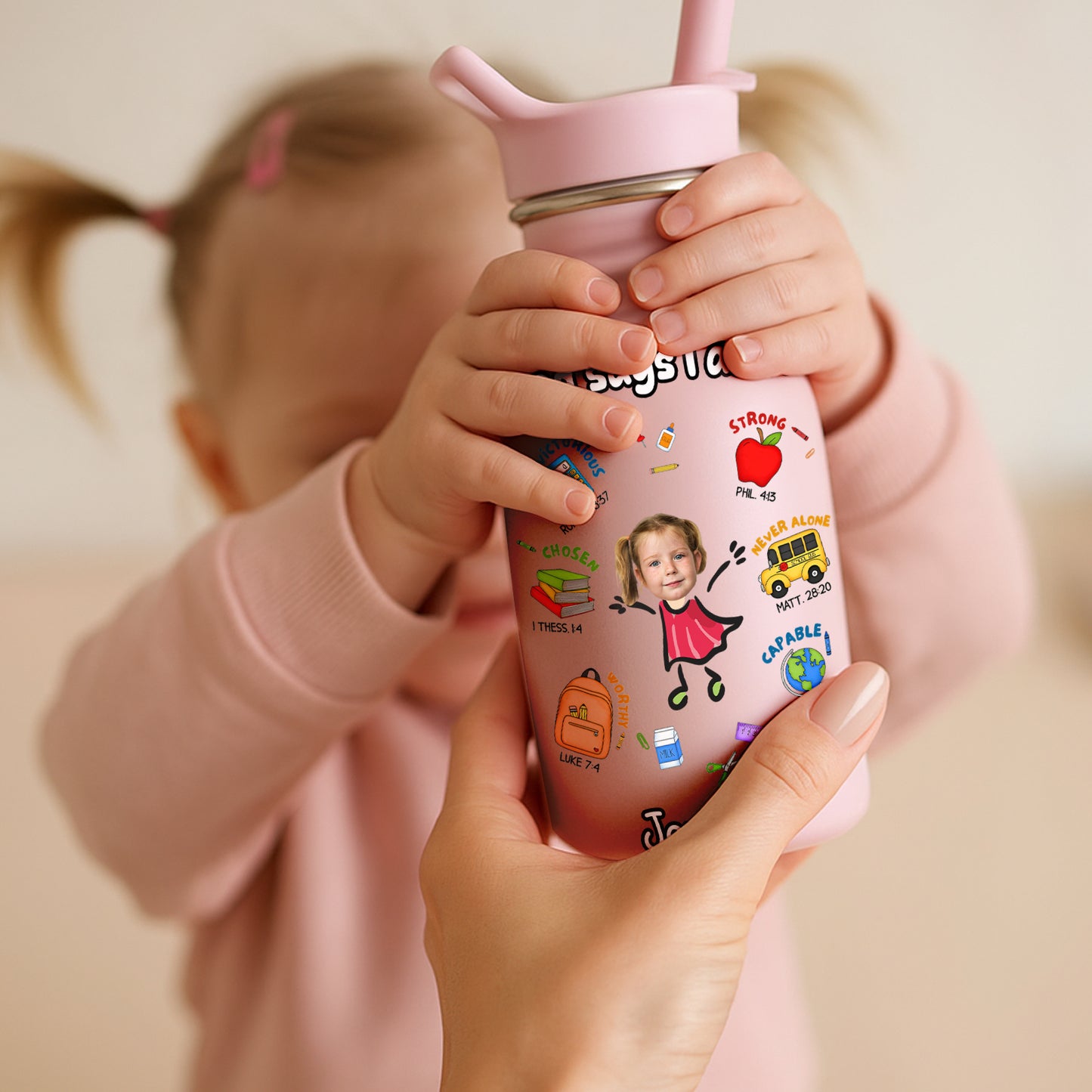 Pink water bottle for kids with colorful cartoon stickers held by child and adult hands