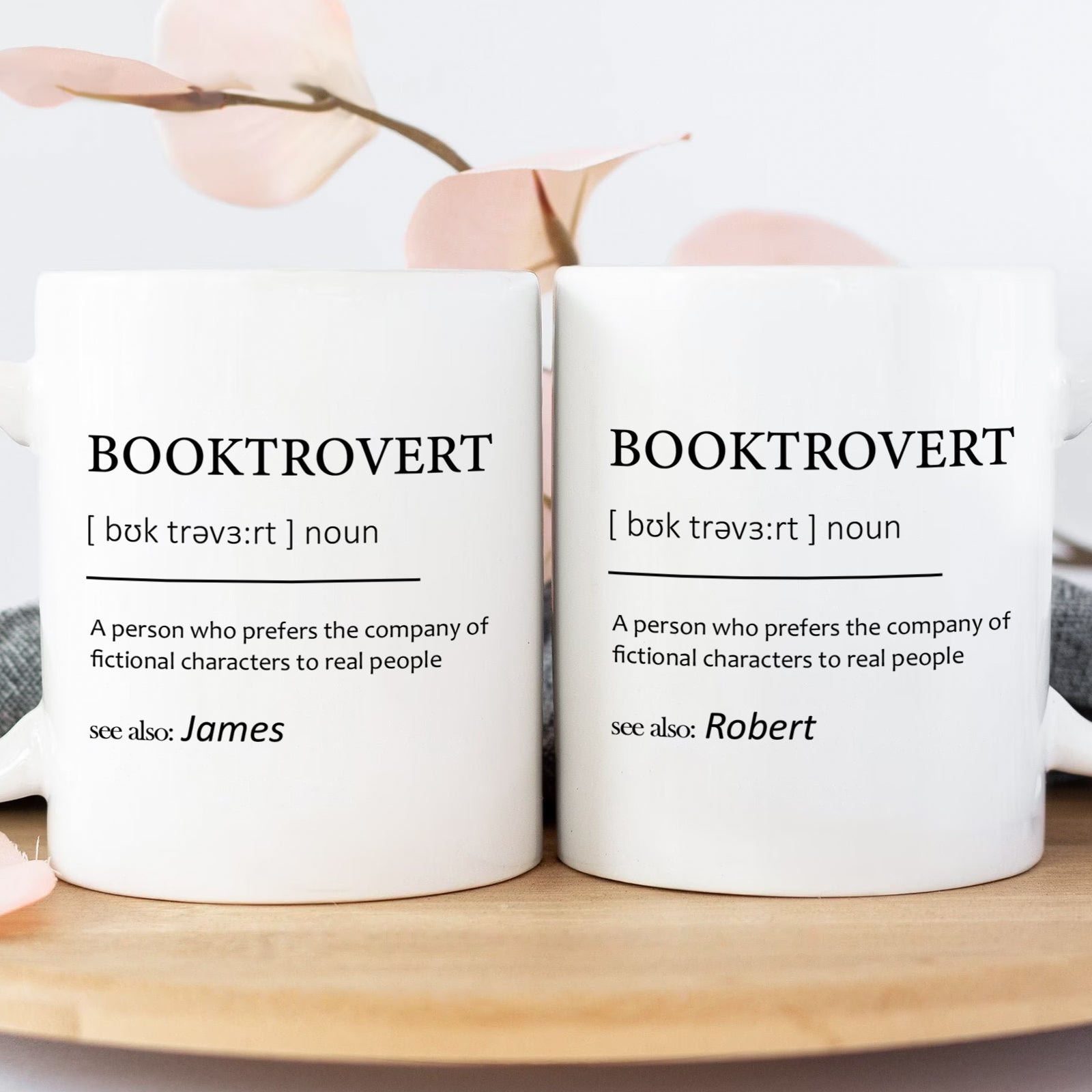 Pair of white personalized booktrovert mug displaying definition print and names James and Robert on wooden tray