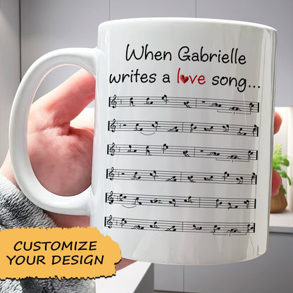 White ceramic romantic custom coffee mug featuring personalized text When Gabrielle writes a love song and printed sheet music
