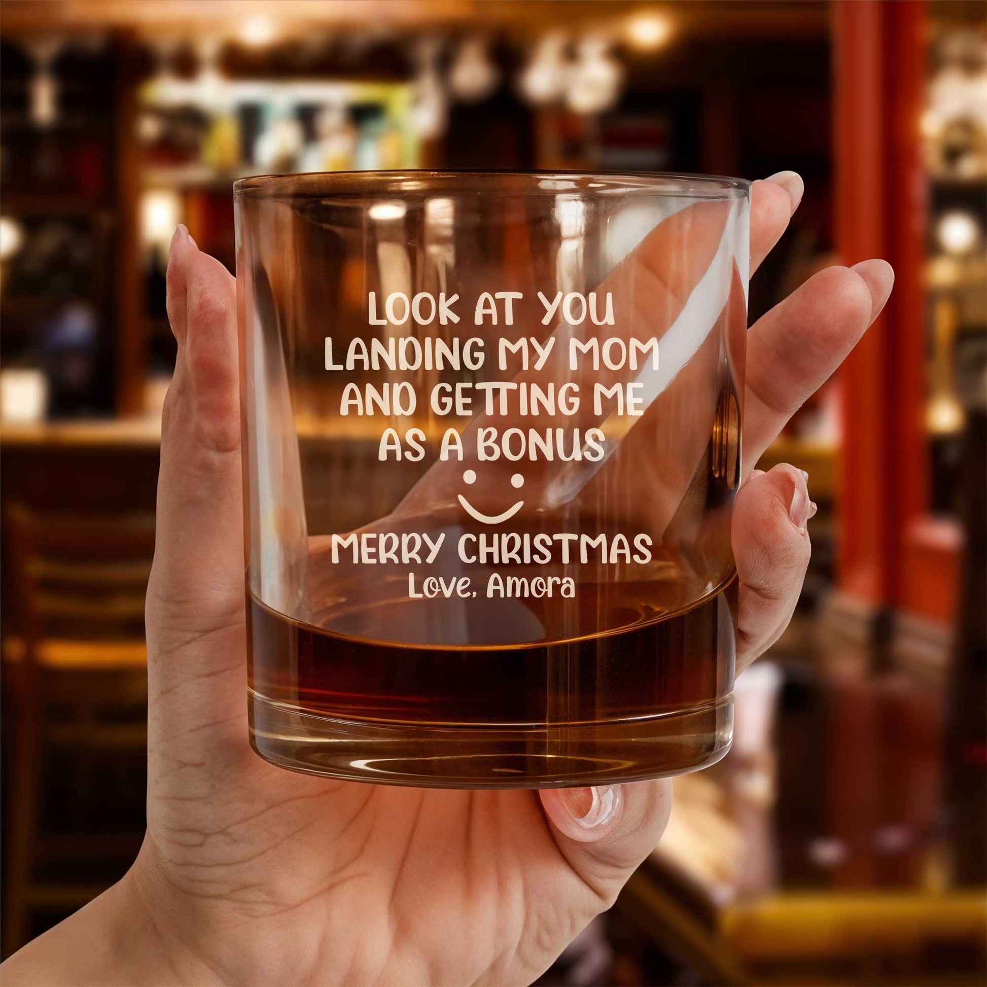 Personalized Whiskey Glass engraved with funny Christmas message held in hand with whiskey in bar setting