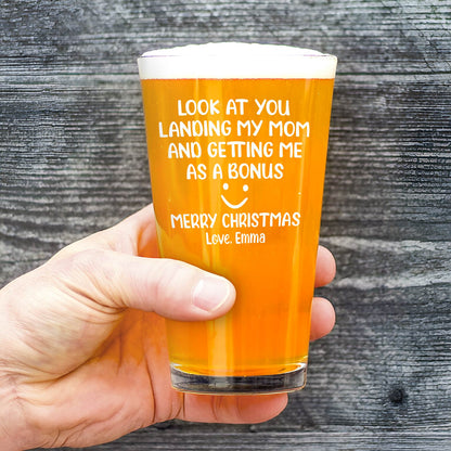 Hand holding engraved pint glass with Merry Christmas message filled with amber beer and foam Personalized Whiskey Glass