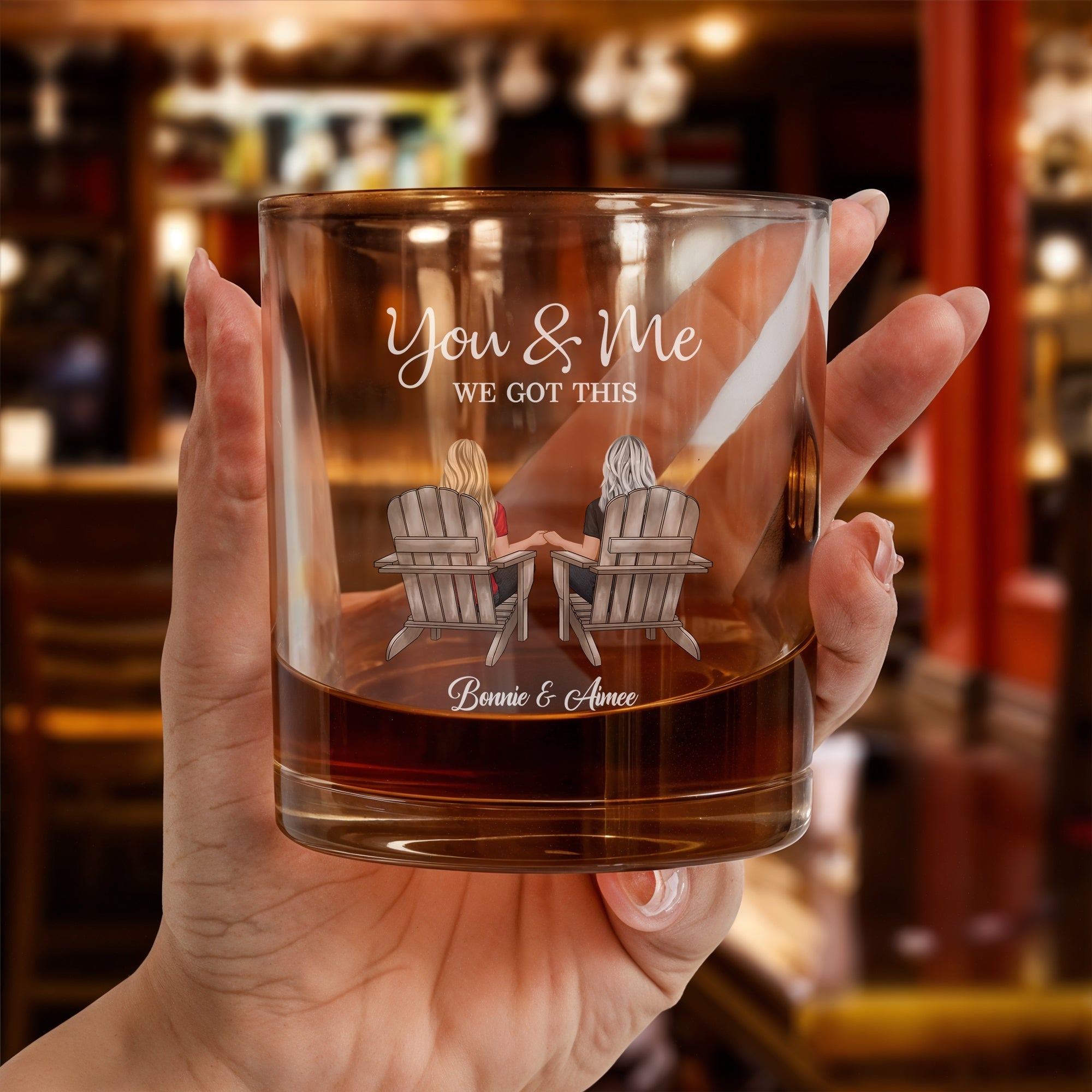 Hand holding a personalized couple whiskey glass with two people in Adirondack chairs You and Me message and custom names