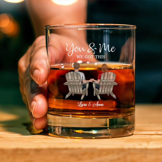 Handheld personalized couple whiskey glass engraved You and Me We Got This with couple in chairs holding hands and custom names