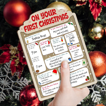 Personalized baby's first Christmas sign with festive notes and colorful holiday icons held against Christmas decorations