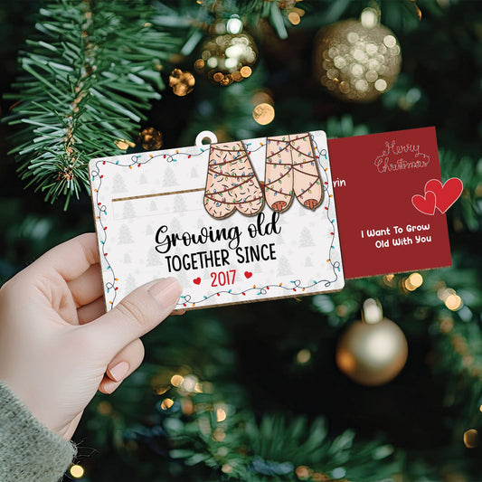 Personalized couples Christmas ornament with stockings and custom text held near decorated Christmas tree