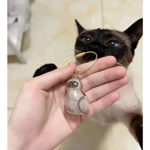 Personalized pet keepsake gift in a cat shape held by a hand with a Siamese cat in the background