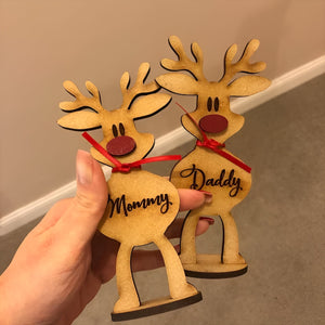 Hand holding two personalized reindeer family decoration wooden ornaments labeled Mommy and Daddy with red ribbons