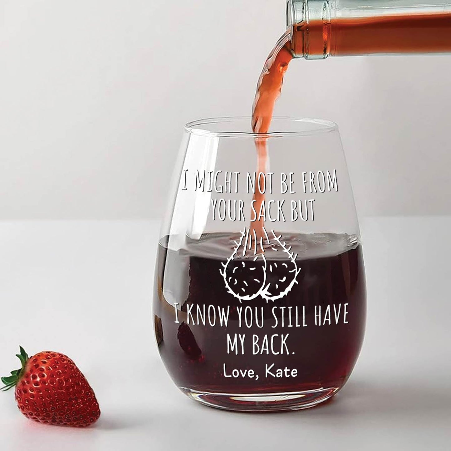 Personalized stepdad wine glass with humorous message being filled with red wine next to a strawberry