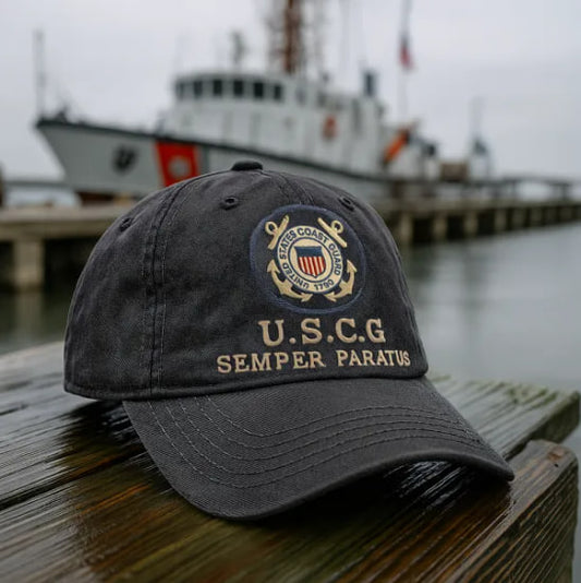Black Semper Paratus Cap featuring U.S. Coast Guard emblem placed on wooden dock near a ship
