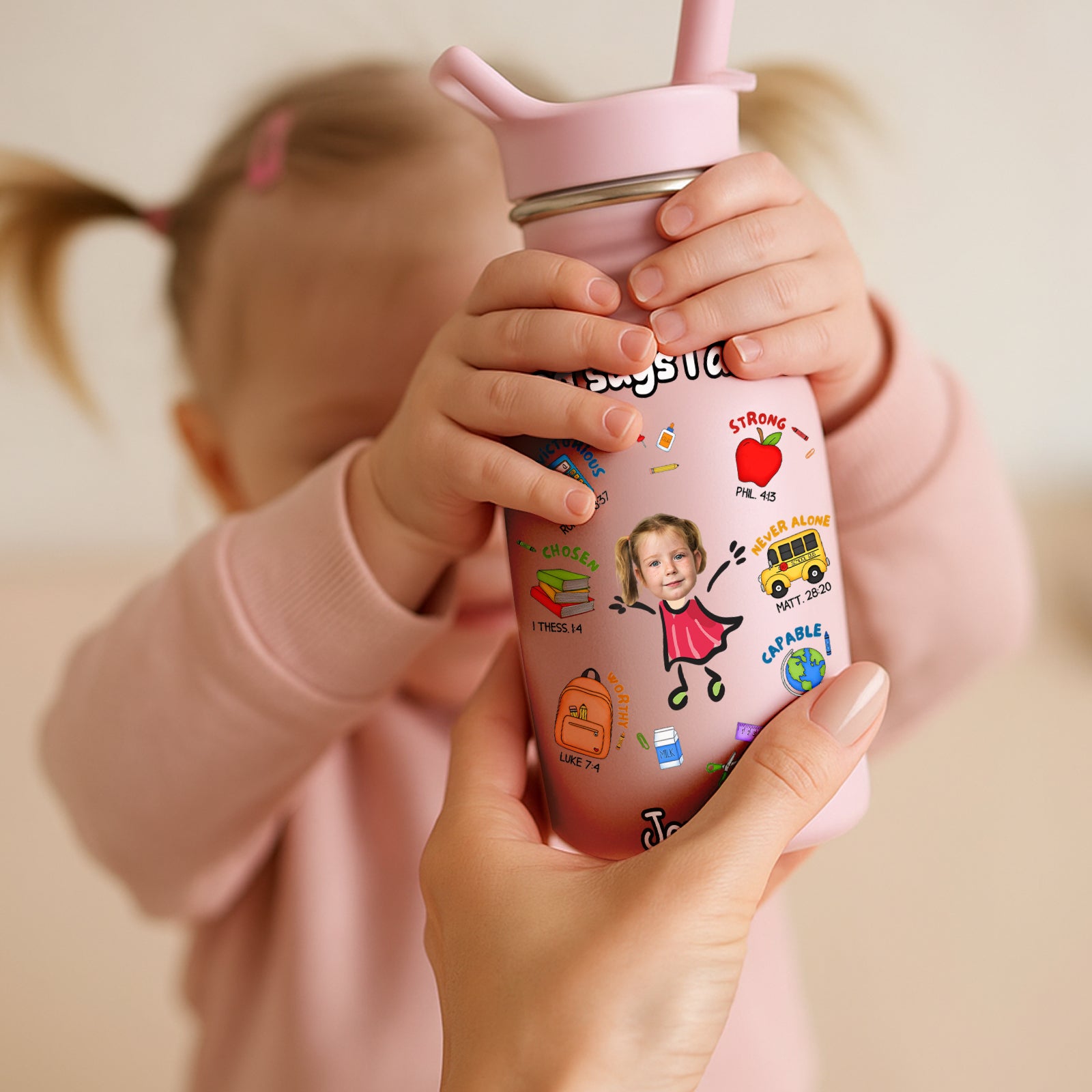 Pink water bottle for kids with colorful cartoon stickers held by child and adult hands